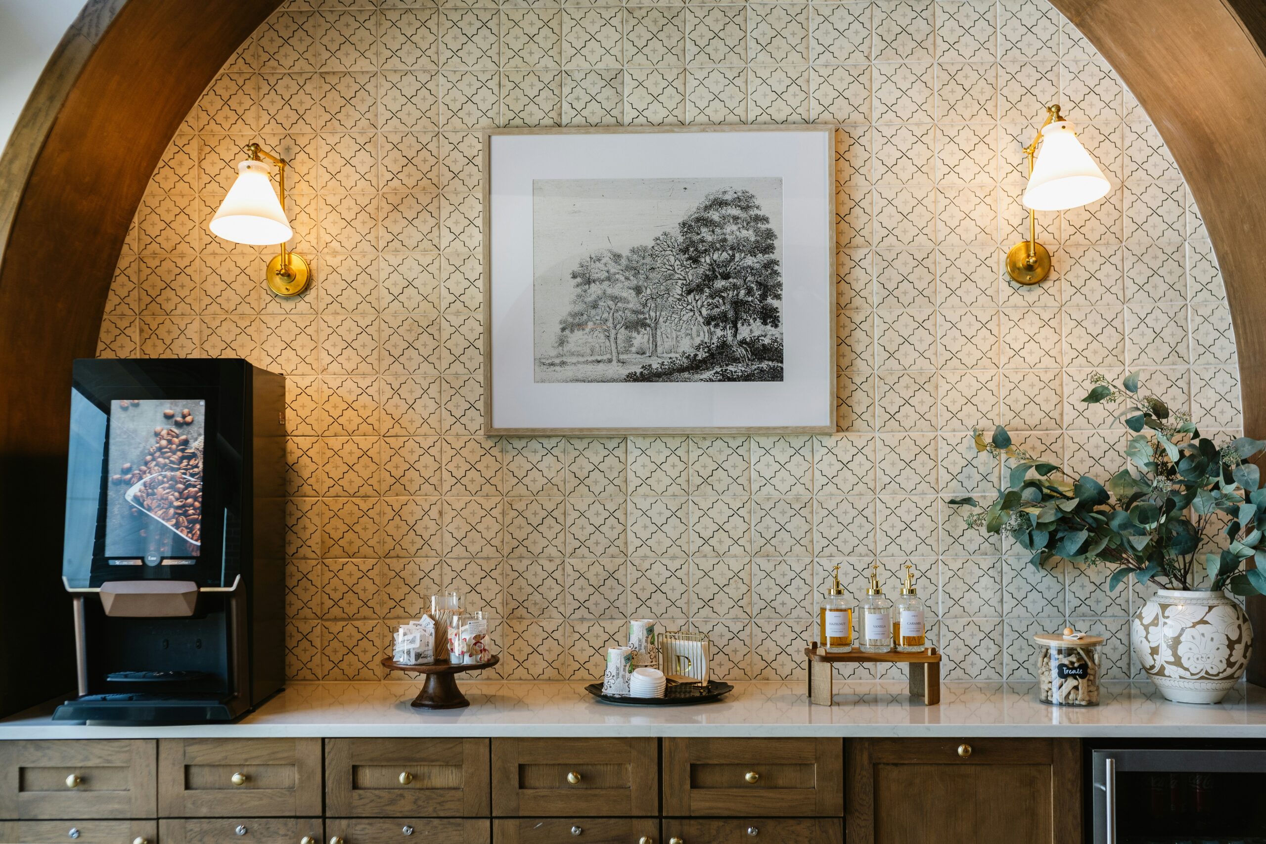 A bean-to-cup coffee machine installed in a stylish hotel or hospitality setting, set within an arched alcove with decorative tiled walls and a marble countertop.