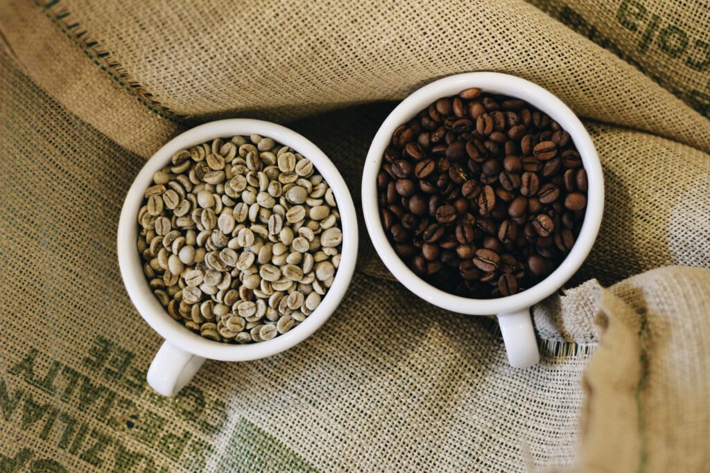 Side-by-side comparison of light roast and dark roast coffee beans in white cups on burlap fabric—light roast on the left showing tan-colored beans, dark roast on the right displaying rich brown beans