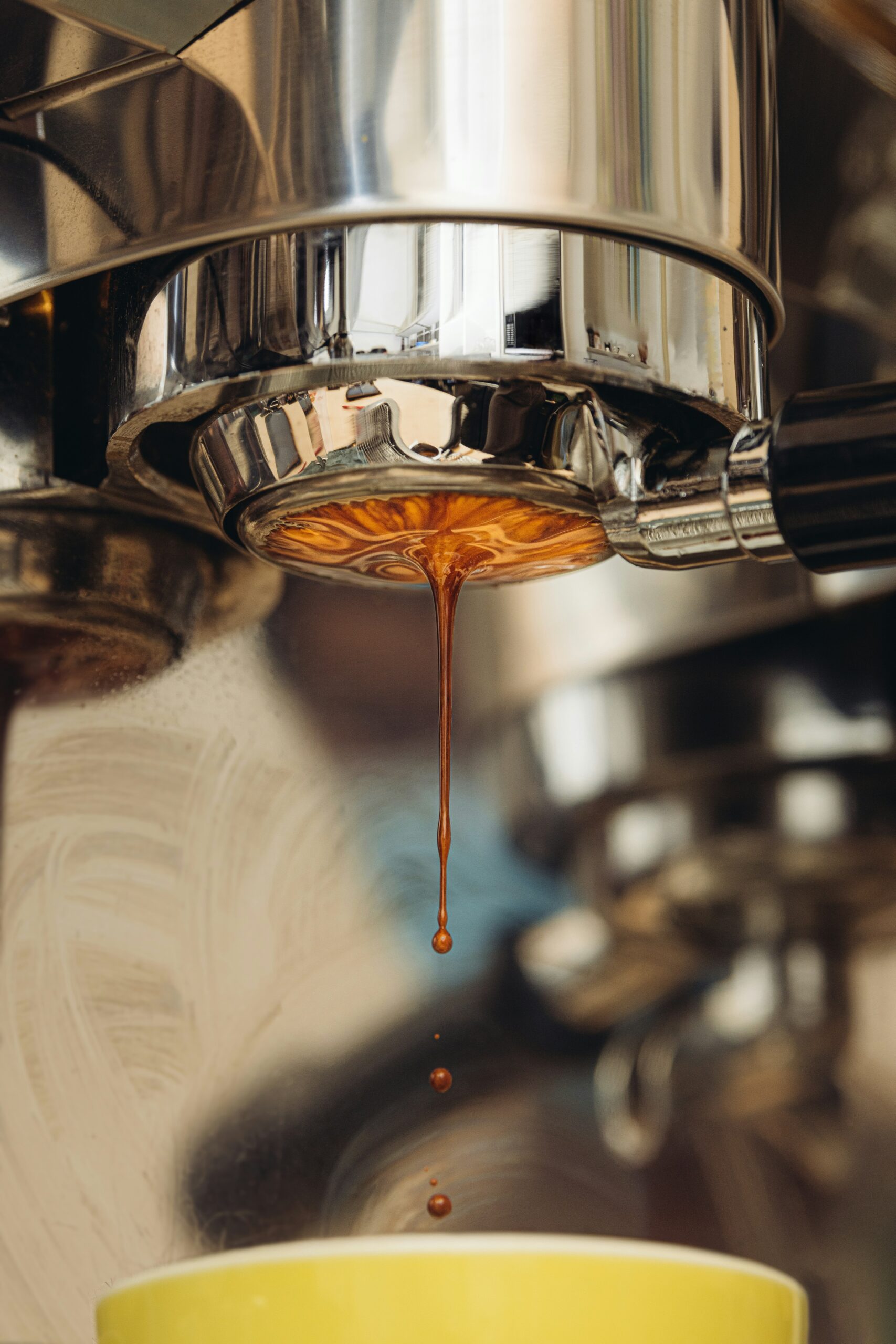 Close-up of rich espresso pouring from a traditional espresso machine group head into a yellow cup, showing the intensity of a freshly pulled shot.